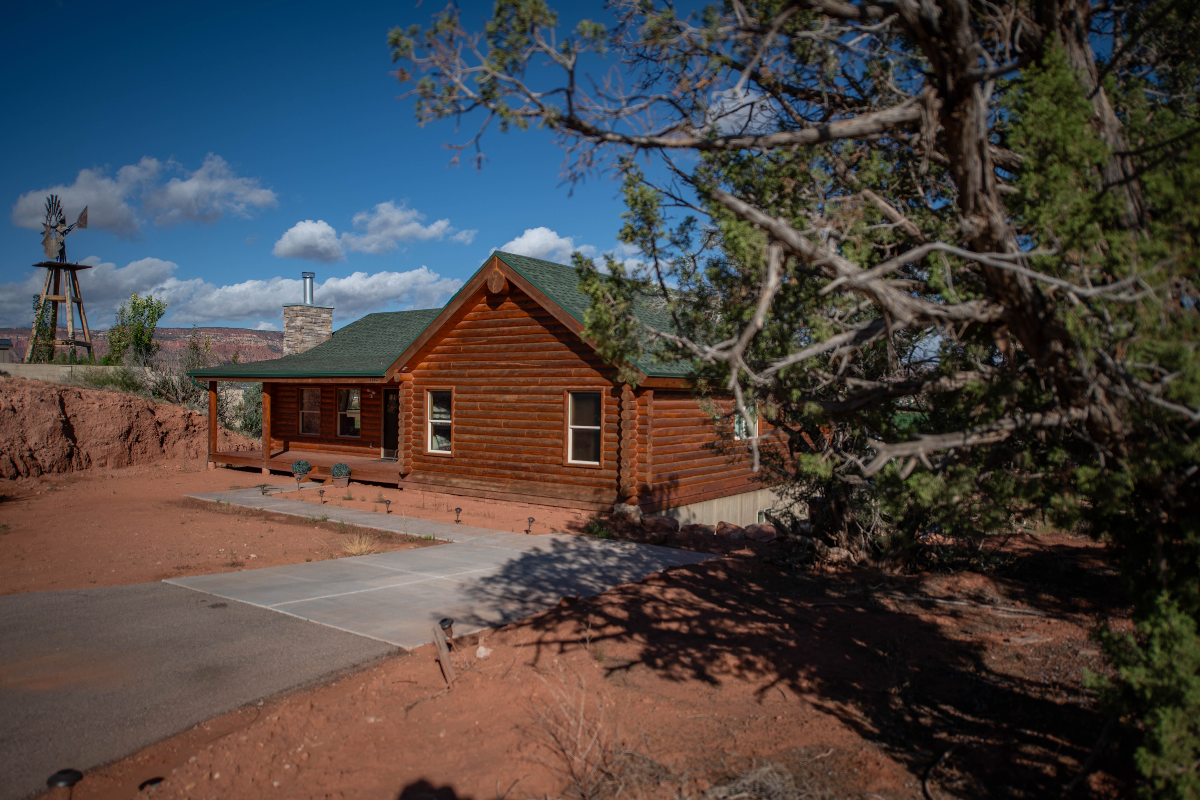 Log cabin exterior in daylight with red rock cliffs and windmill — Kanab Utah
